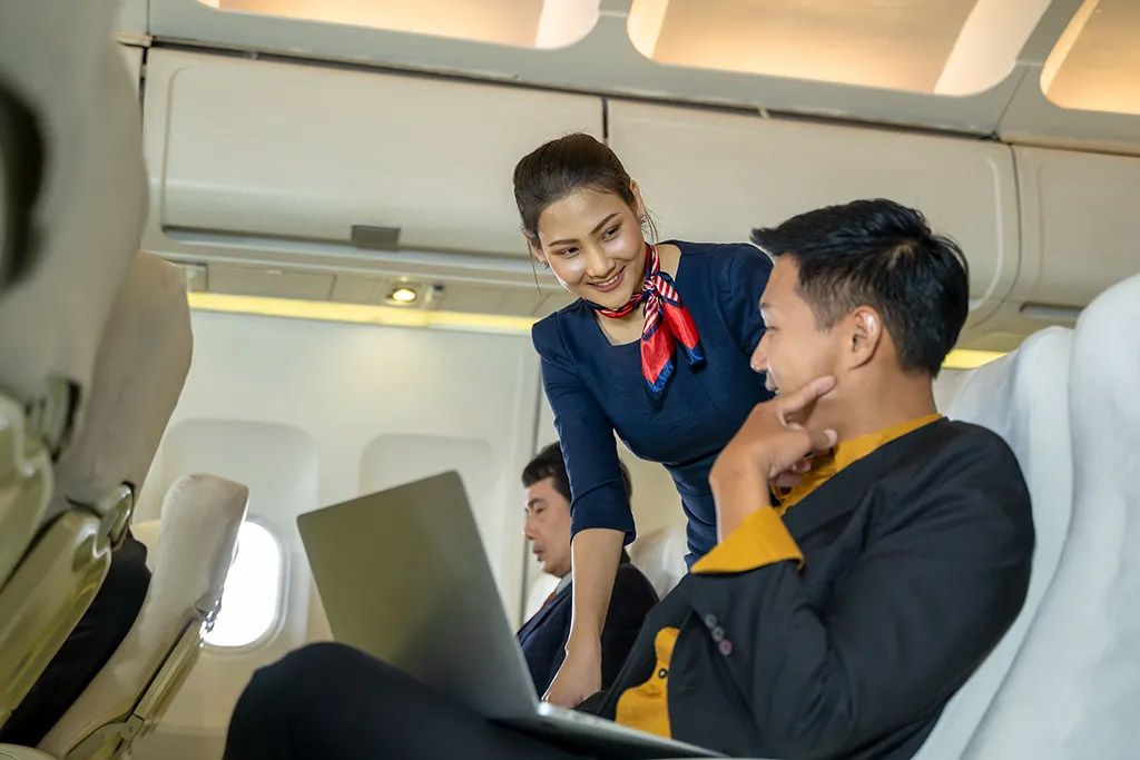Frankfinn cabin crew training student in blue uniform assisting a passenger on flight, showing in-flight service skills.