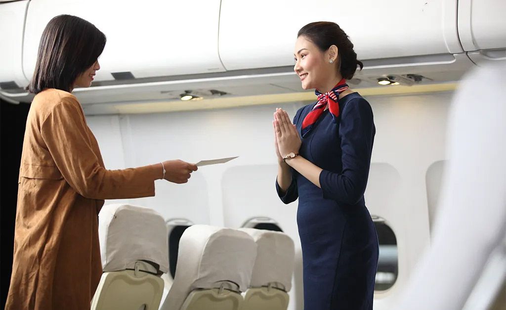 Frankfinn cabin crew training student in blue uniform greeting passenger with namaste on flight, showing hospitality and service skills.